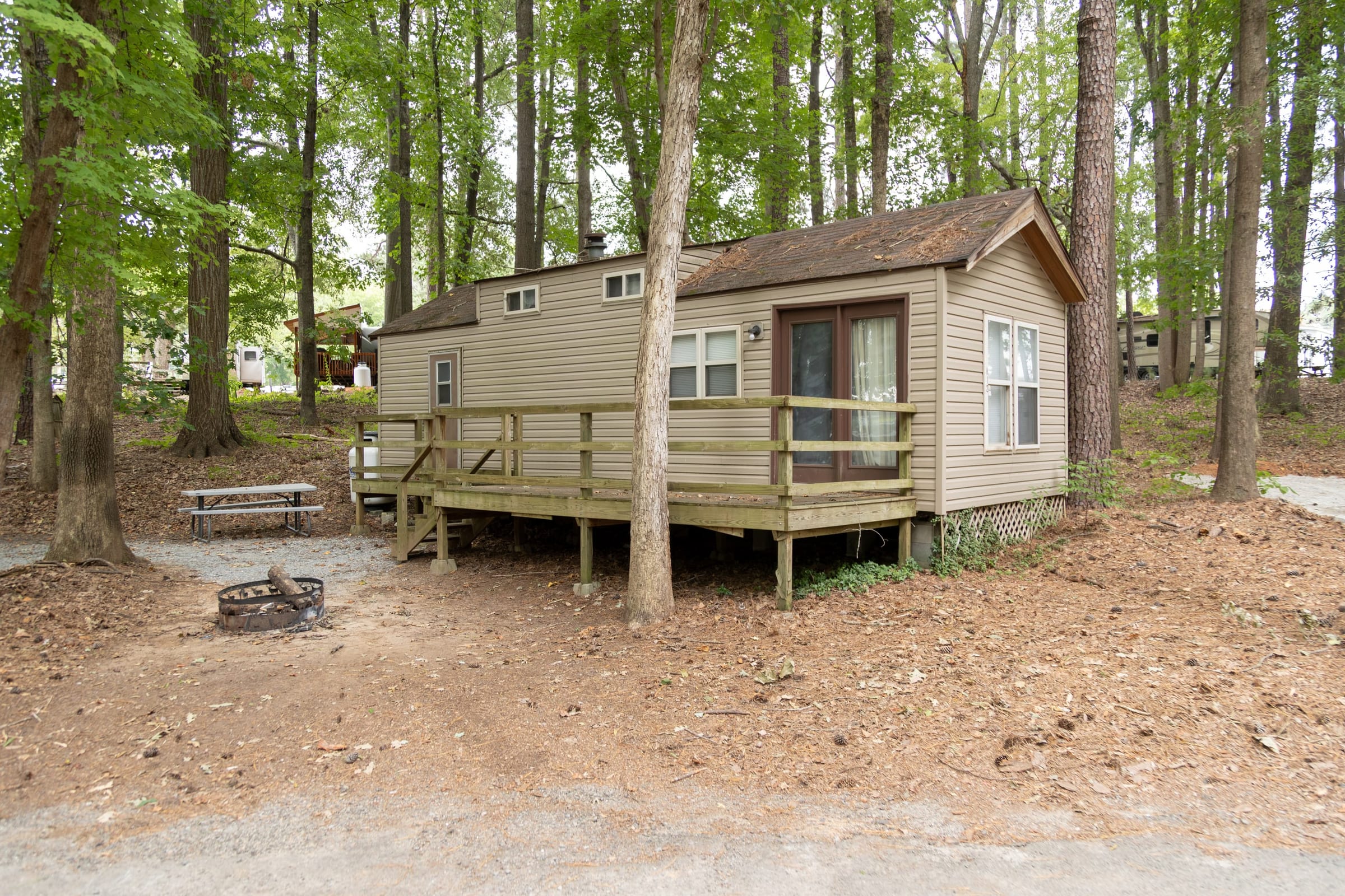 Tan rental cottage with wraparound deck and fire ring in the woods