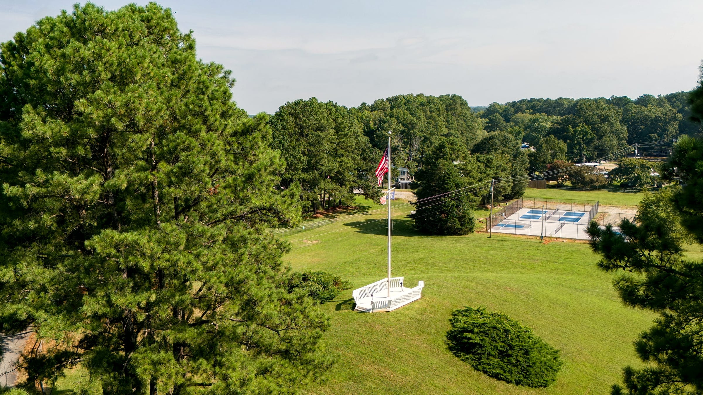 Morning sun across the open event lawn to the flag knoll, pickleball courts beyond
