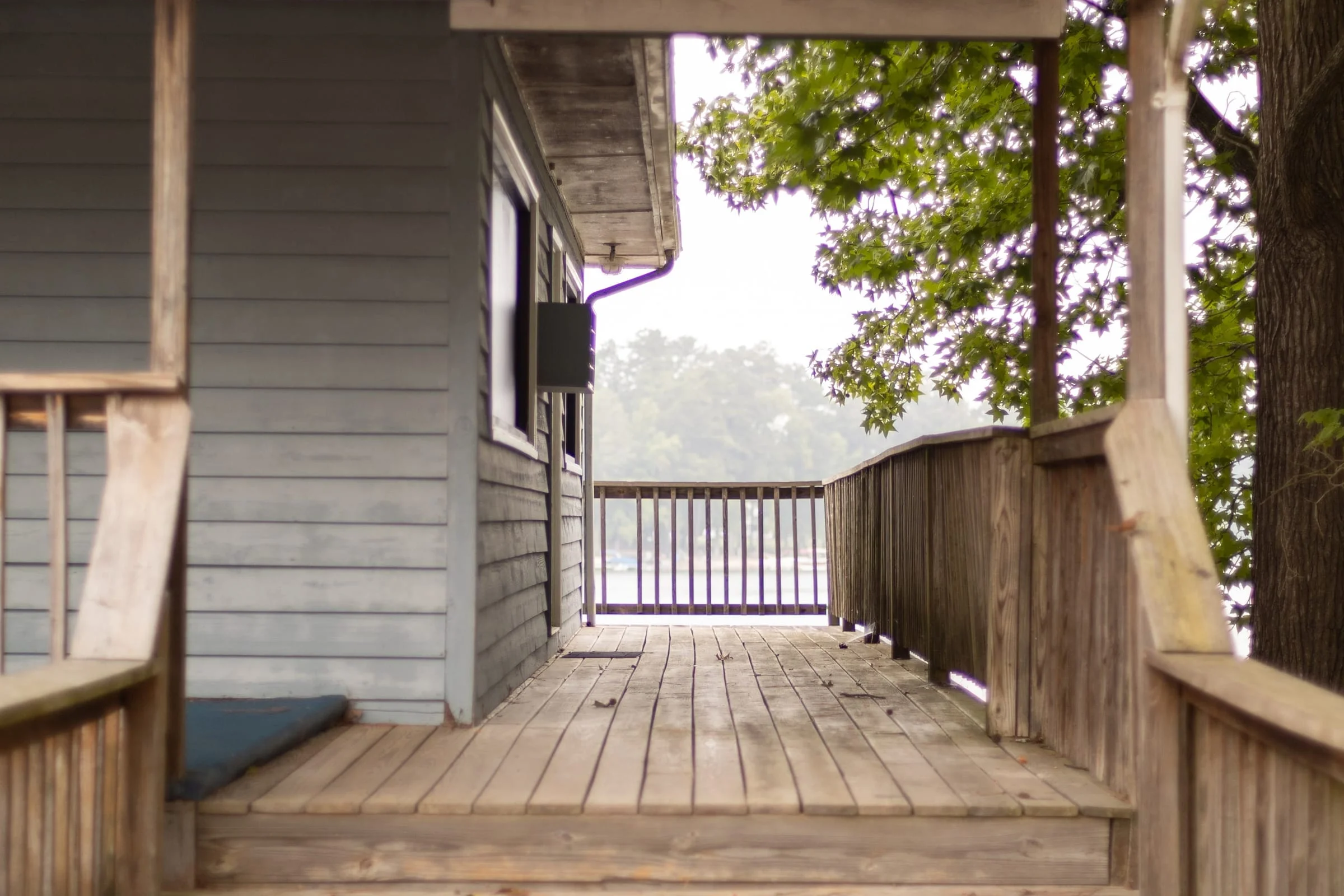 Covered wooden walkway with steps leading toward the water beside a gray building