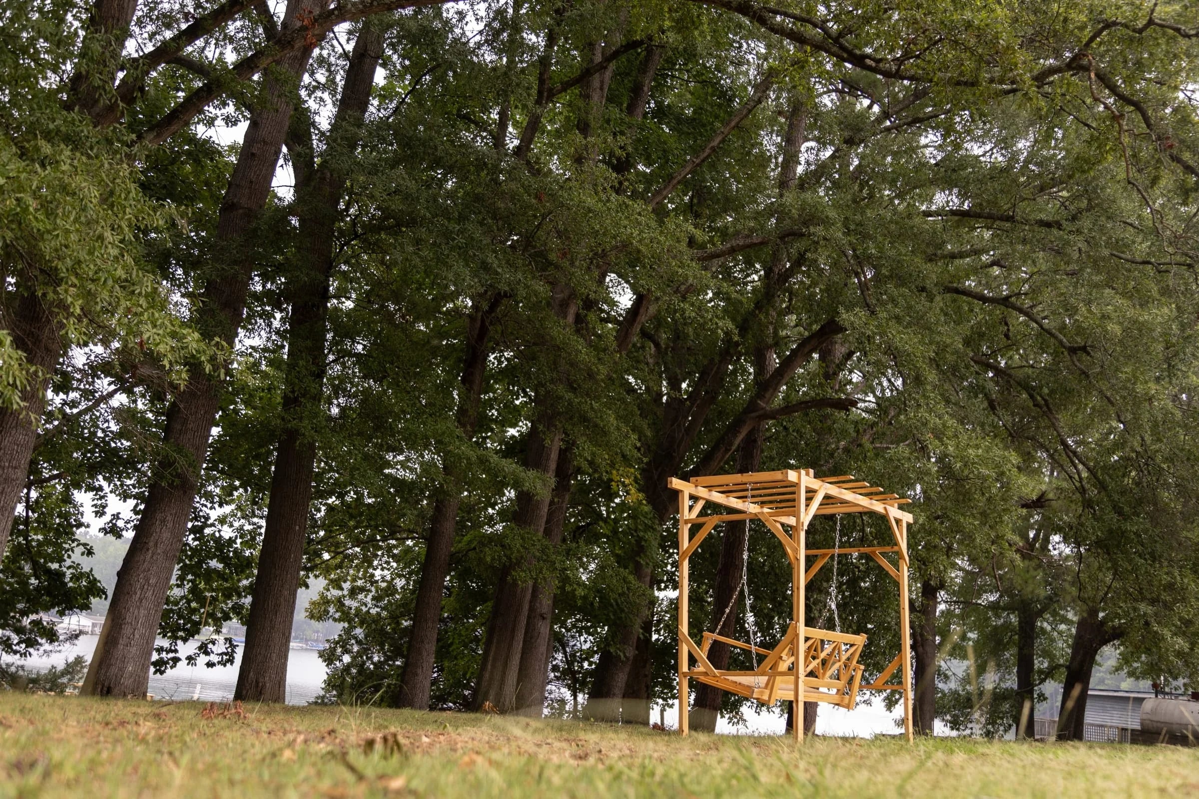 Pergola swing on the shaded lakeside lawn under big trees